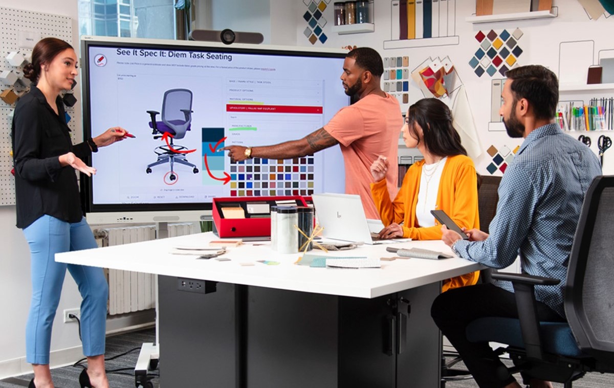  team collaborates in a modern office space, with one member pointing at a SMART Interactive display showing product design specifications.